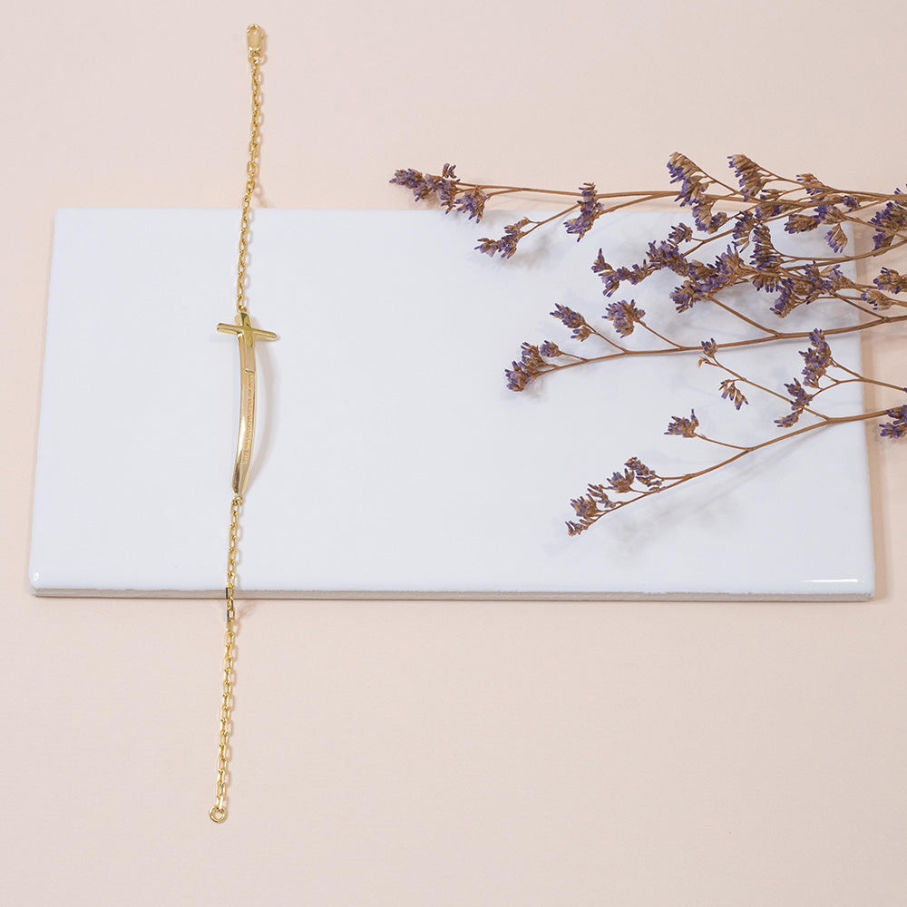 Pulseira Cristã Espada de Dois Gumes Masculino em Prata de Lei com banho de ouro 18kt em cima de azulejo branco com um fundo rosa bem claro e flores secas ao lado